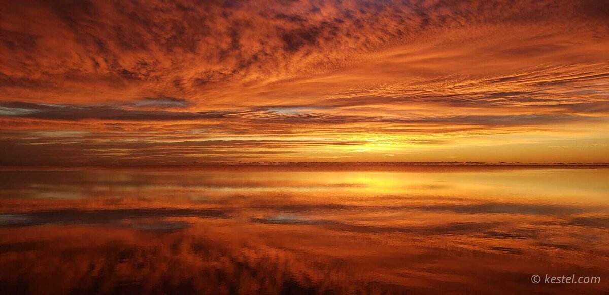 Deep crimson sunrise reflected in mirror-calm water
