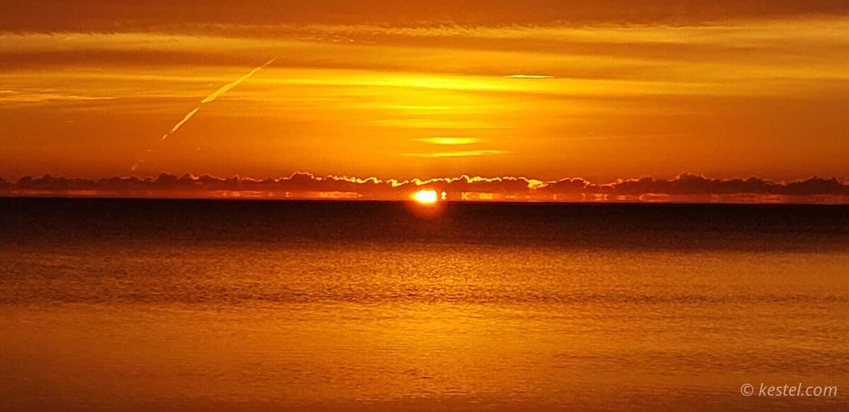 Golden sunrise with aircraft contrail streaking across the sky