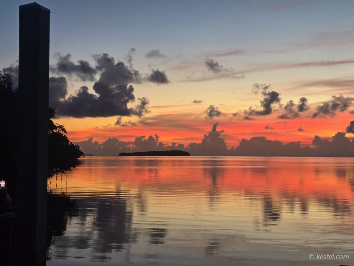 Calm bay at sunset with island silhouette and vivid sky reflection
