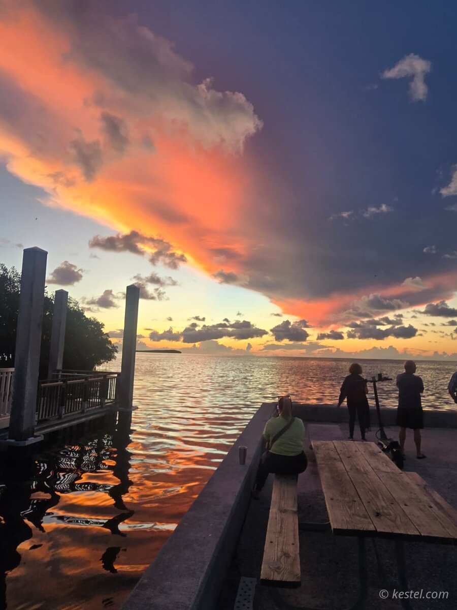 Vivid orange and purple sunset over water with people at a dock