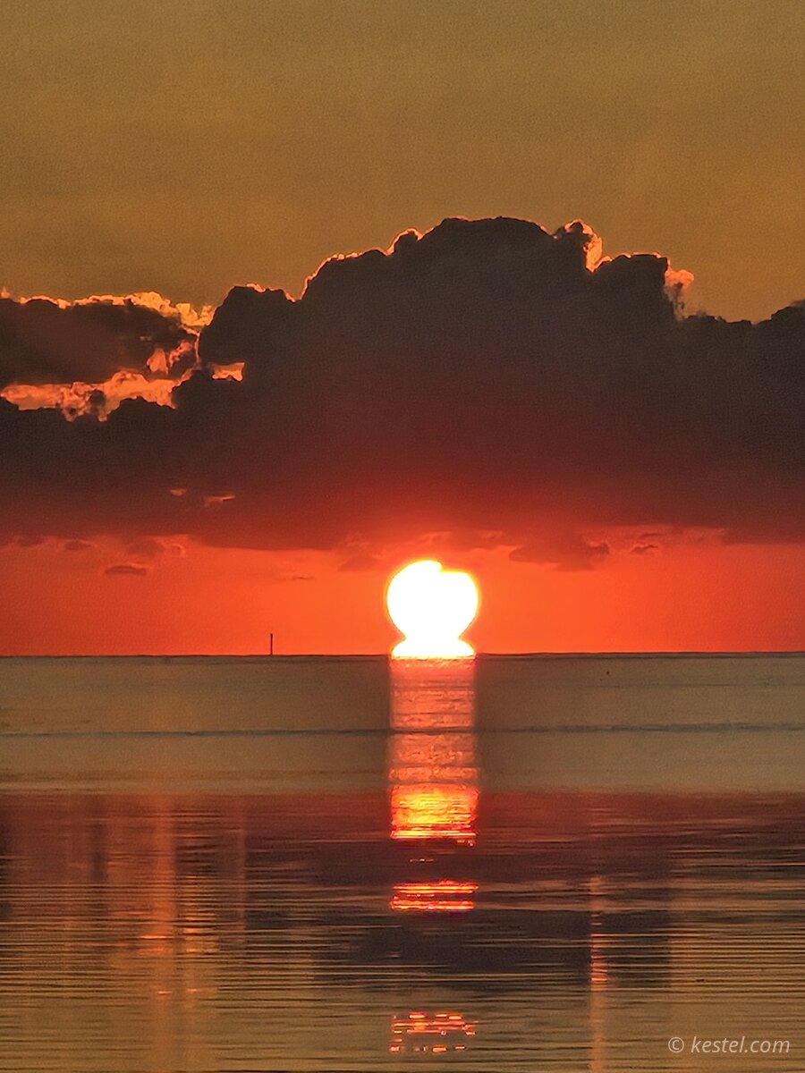 Sun touching the horizon at sunset over water