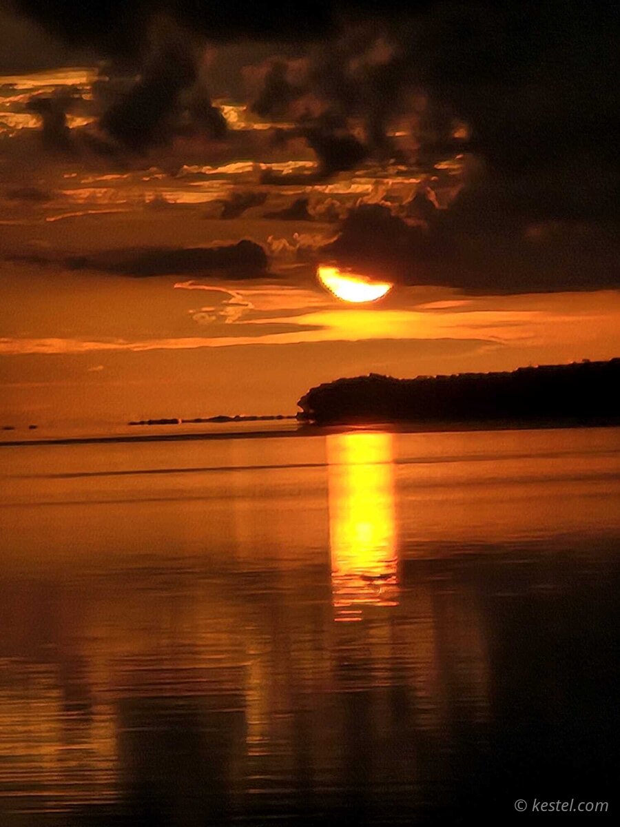Crescent sun rising through clouds reflected in bay
