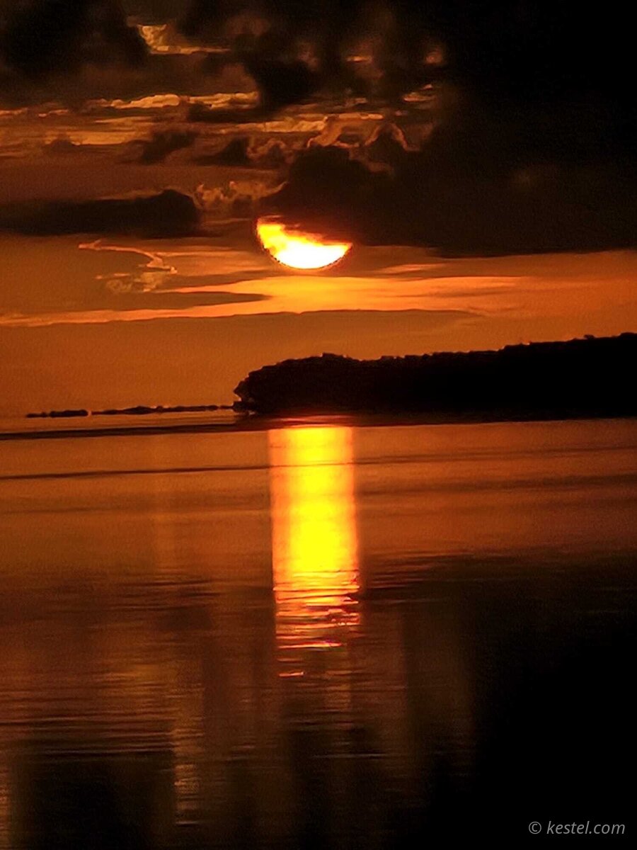 Half-crescent sun emerging through storm clouds at sunrise